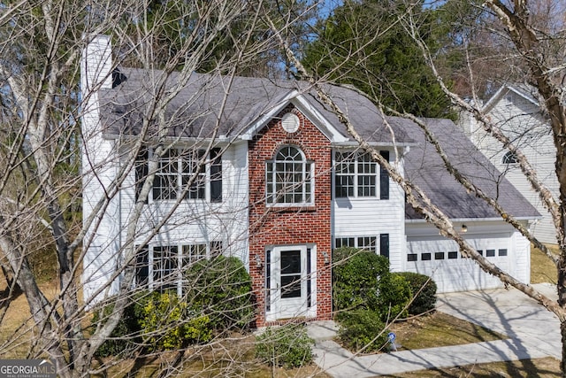 colonial-style house featuring driveway, roof with shingles, an attached garage, brick siding, and a chimney