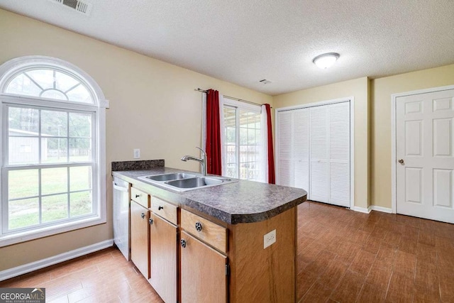 kitchen with a sink, dark countertops, wood finished floors, a peninsula, and dishwasher