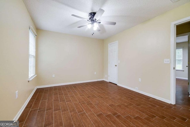 empty room featuring ceiling fan, baseboards, a textured ceiling, and dark wood-style floors