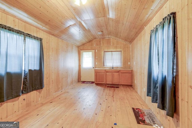 empty room with light wood finished floors, wood walls, wood ceiling, and vaulted ceiling