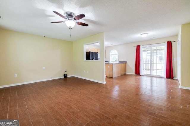 unfurnished living room with ceiling fan, a textured ceiling, baseboards, and wood finished floors