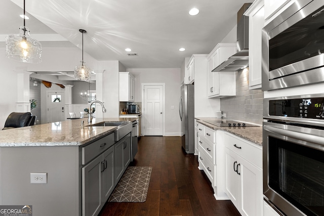 kitchen with gray cabinetry, dark wood-type flooring, stainless steel appliances, wall chimney exhaust hood, and a sink