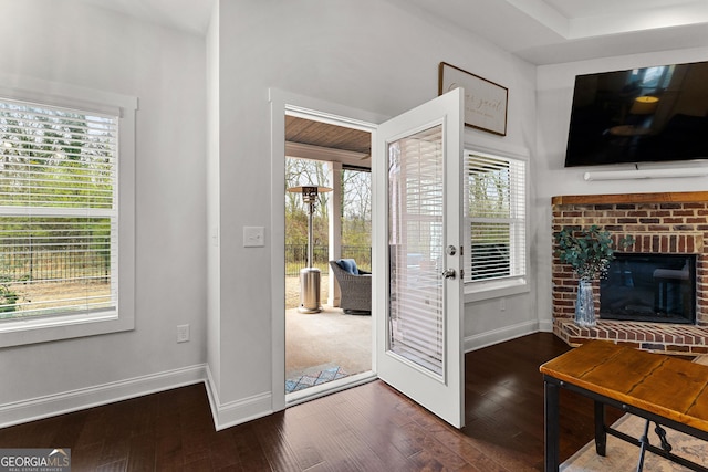 doorway to outside featuring dark wood finished floors, a brick fireplace, and baseboards