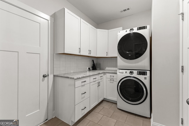 washroom featuring visible vents, cabinet space, light tile patterned flooring, and stacked washing maching and dryer