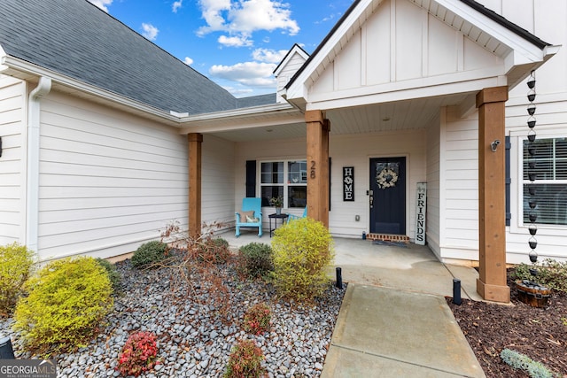 doorway to property with covered porch, board and batten siding, and roof with shingles