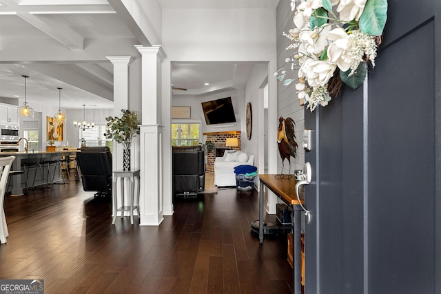 foyer entrance with beamed ceiling, a notable chandelier, dark wood-style floors, and ornate columns