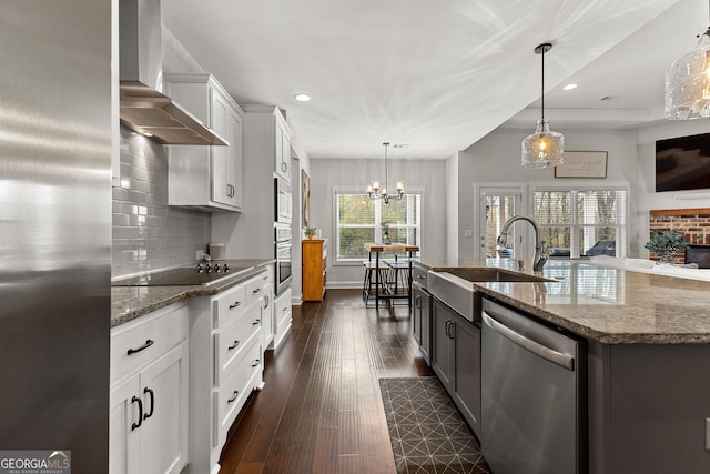 kitchen with light stone countertops, a sink, stainless steel appliances, wall chimney exhaust hood, and backsplash