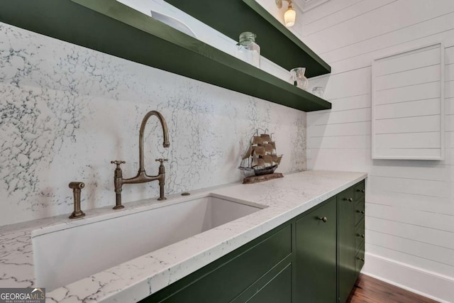 kitchen with green cabinets, open shelves, light stone countertops, and a sink