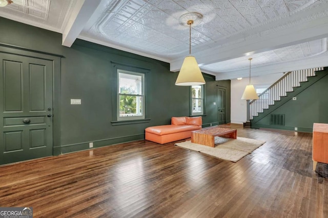 unfurnished living room featuring hardwood / wood-style floors, stairway, visible vents, baseboards, and beamed ceiling