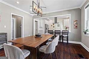 dining area with dark wood-style floors, baseboards, an inviting chandelier, and ornamental molding