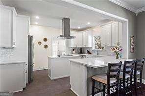 kitchen featuring freestanding refrigerator, light countertops, white cabinets, a kitchen breakfast bar, and wall chimney exhaust hood