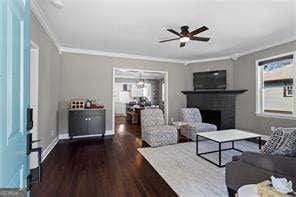 living area featuring baseboards, ceiling fan, ornamental molding, a fireplace, and wood finished floors