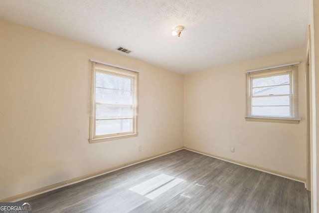 spare room with baseboards, wood finished floors, visible vents, and a textured ceiling