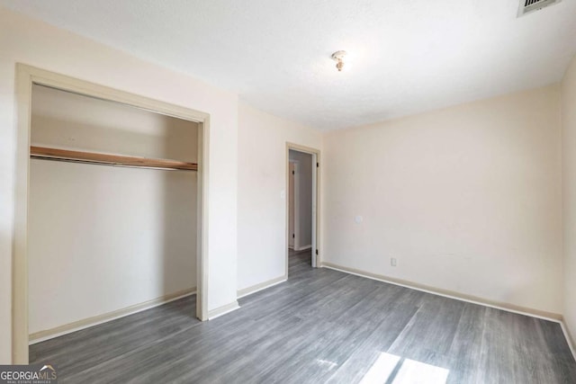 unfurnished bedroom featuring visible vents, baseboards, a closet, and wood finished floors