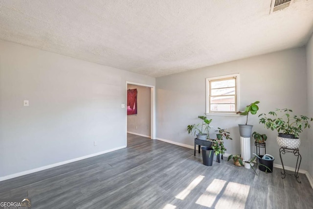 empty room with dark wood finished floors, visible vents, a textured ceiling, and baseboards