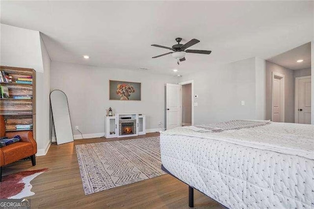 bedroom featuring wood finished floors, baseboards, recessed lighting, a warm lit fireplace, and ceiling fan