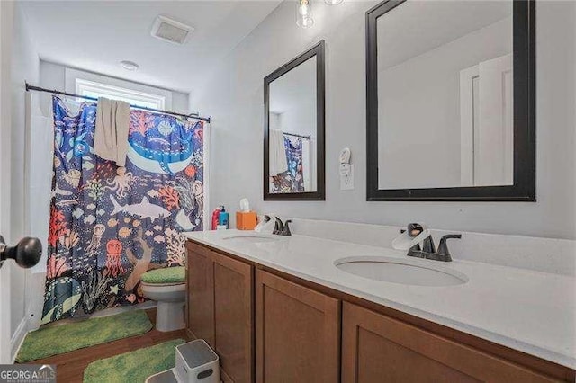 full bath with a sink, visible vents, toilet, and double vanity