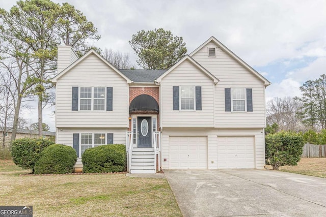 raised ranch with a front lawn, concrete driveway, an attached garage, brick siding, and a chimney