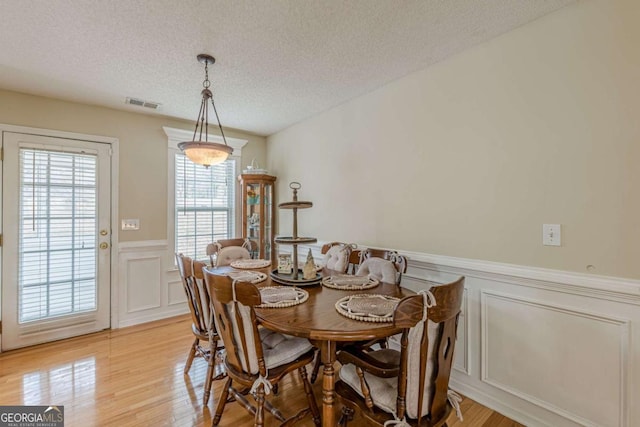 dining area featuring visible vents, wainscoting, light wood-style floors, a decorative wall, and a textured ceiling