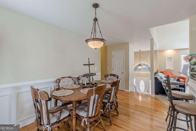 dining room with light wood-type flooring, a notable chandelier, a wainscoted wall, and a textured ceiling