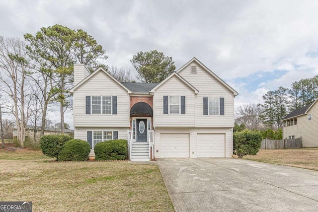 bi-level home featuring brick siding, concrete driveway, a front yard, a chimney, and an attached garage