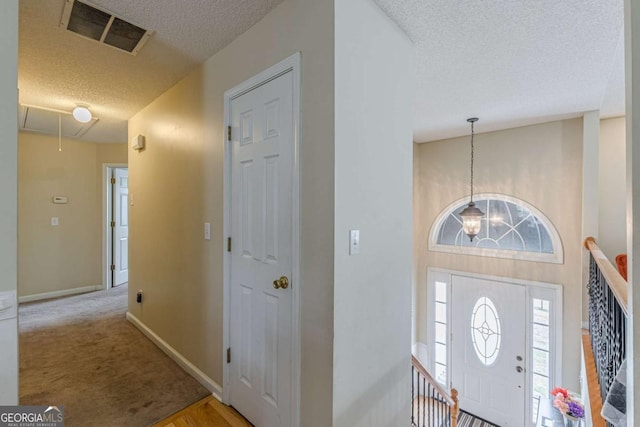 entrance foyer featuring visible vents, carpet flooring, a textured ceiling, and baseboards