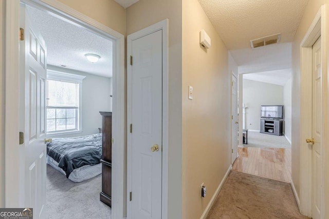 hallway featuring visible vents, carpet floors, a textured ceiling, and baseboards