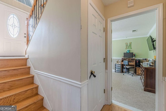 staircase with a wainscoted wall, a textured ceiling, visible vents, and ornamental molding