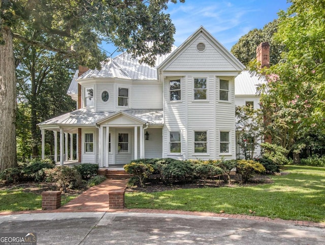 victorian house with metal roof, a porch, and a front yard