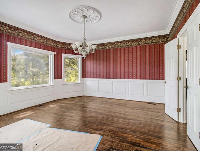 unfurnished dining area with visible vents, wood finished floors, an inviting chandelier, wainscoting, and wallpapered walls