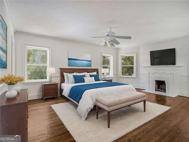 bedroom featuring a fireplace with flush hearth, wood finished floors, crown molding, baseboards, and ceiling fan