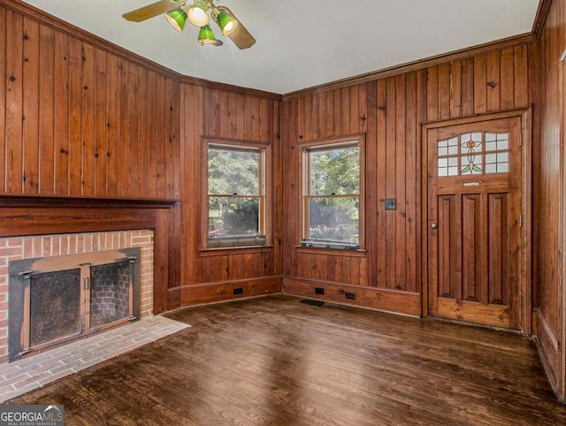 unfurnished living room featuring wooden walls, ceiling fan, ornamental molding, a fireplace, and wood finished floors