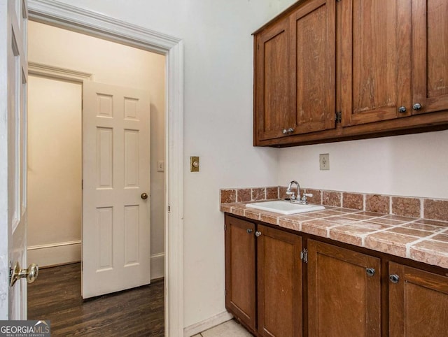 kitchen with dark wood-type flooring, brown cabinetry, baseboards, and a sink