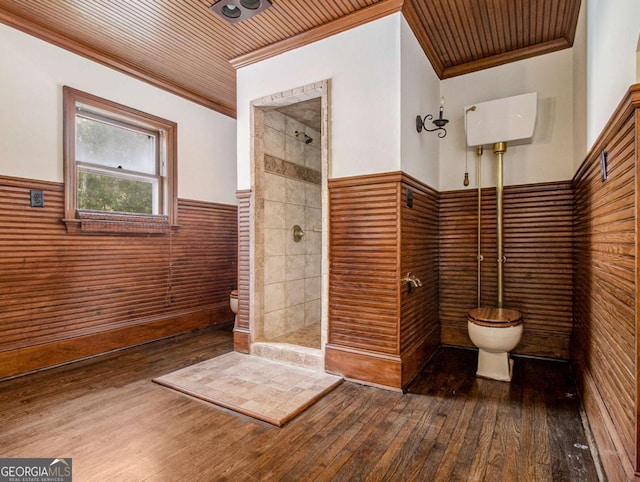 bathroom featuring a wainscoted wall, toilet, hardwood / wood-style floors, a tile shower, and crown molding