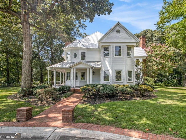 victorian home featuring a standing seam roof, a front lawn, covered porch, and metal roof