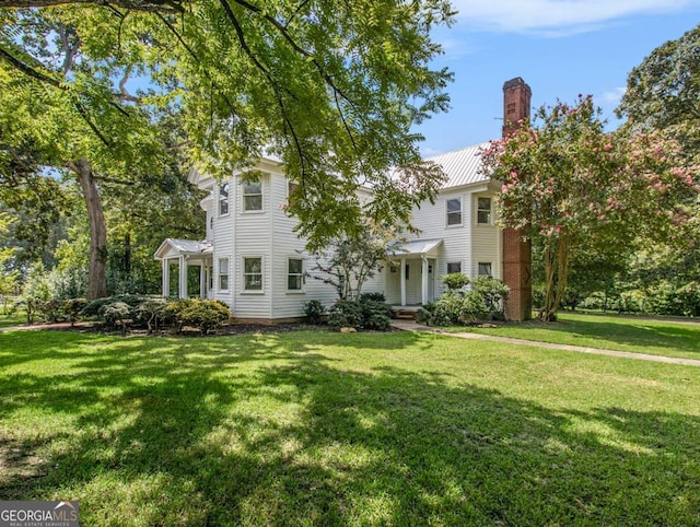 view of front facade with a front yard, metal roof, and a chimney