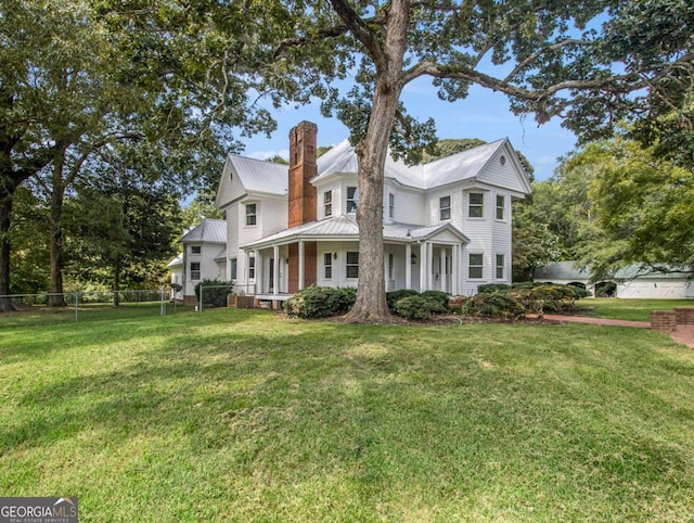 view of front of property with a front lawn, fence, covered porch, metal roof, and a chimney