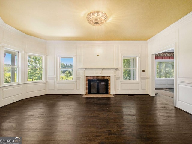 unfurnished living room with a brick fireplace, ornamental molding, dark wood-style flooring, and a decorative wall