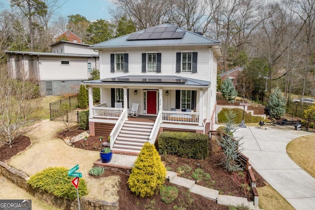 view of front of property featuring driveway, covered porch, stairs, roof mounted solar panels, and metal roof