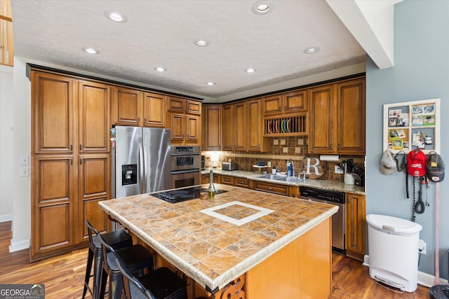 kitchen featuring a center island, wood finished floors, brown cabinetry, stainless steel appliances, and a sink