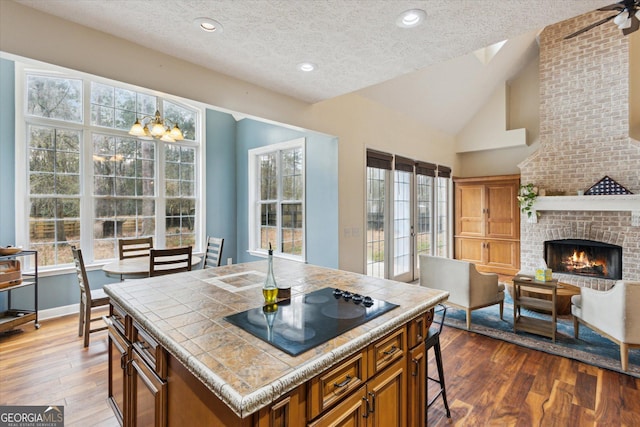 kitchen featuring a brick fireplace, black electric stovetop, brown cabinets, and tile counters