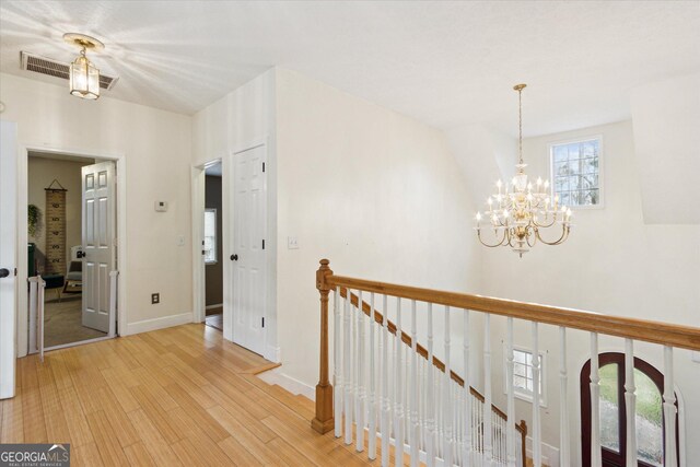 corridor featuring visible vents, baseboards, light wood-style floors, a notable chandelier, and an upstairs landing