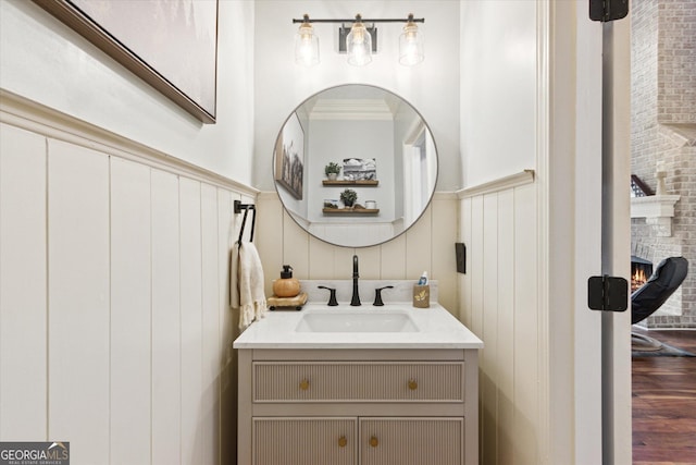 bathroom featuring wainscoting, a fireplace, vanity, and wood finished floors