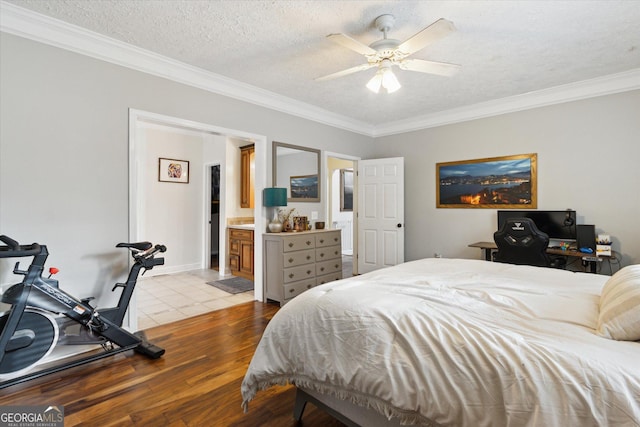 bedroom with a ceiling fan, wood finished floors, ornamental molding, a textured ceiling, and connected bathroom