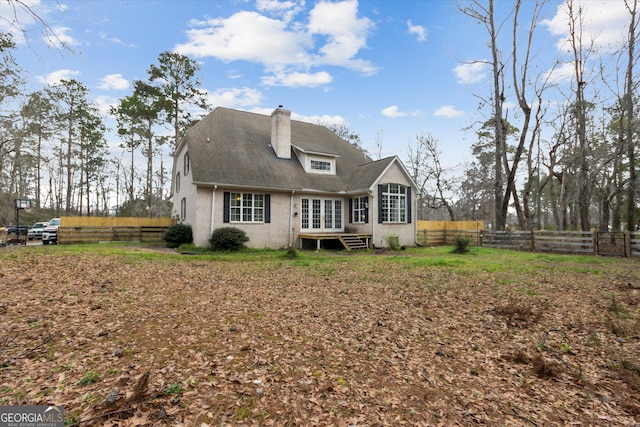 rear view of house with entry steps, fence, brick siding, and a chimney