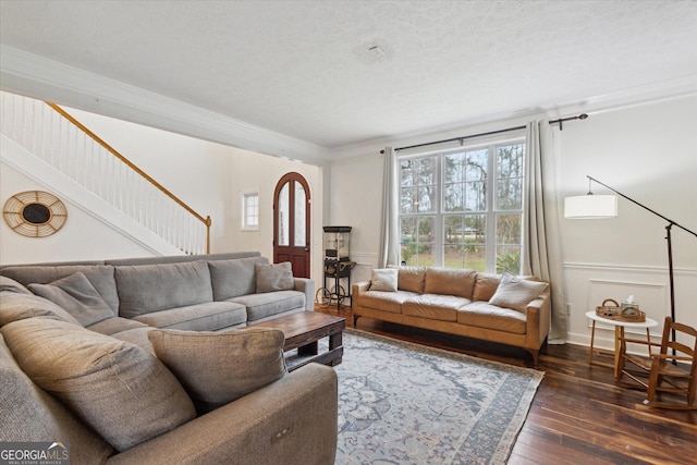 living area featuring a wainscoted wall, dark wood-type flooring, a textured ceiling, crown molding, and stairs