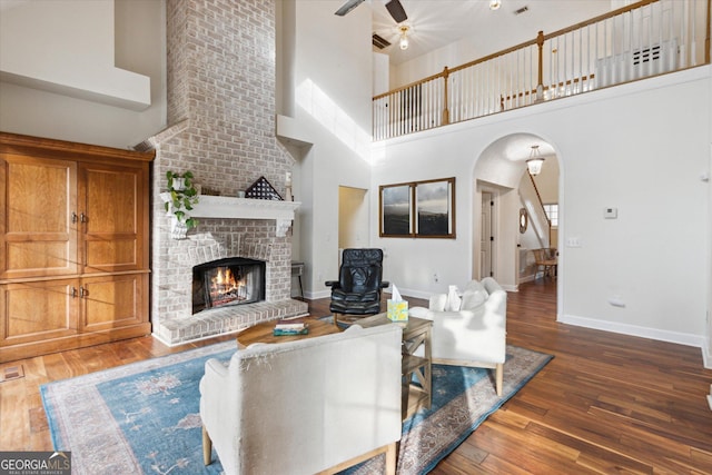 living area with baseboards, a fireplace, arched walkways, ceiling fan, and hardwood / wood-style flooring