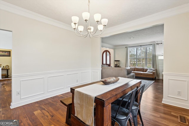 dining space featuring visible vents, crown molding, a wainscoted wall, an inviting chandelier, and wood finished floors