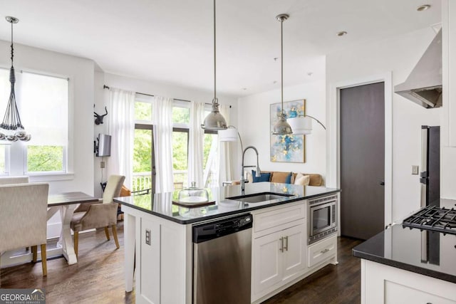 kitchen with dark countertops, stainless steel appliances, wall chimney range hood, and a sink