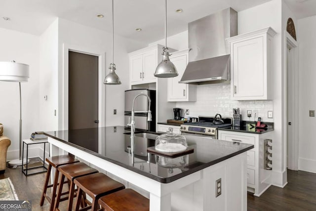 kitchen with dark wood finished floors, stainless steel appliances, decorative backsplash, dark countertops, and wall chimney exhaust hood